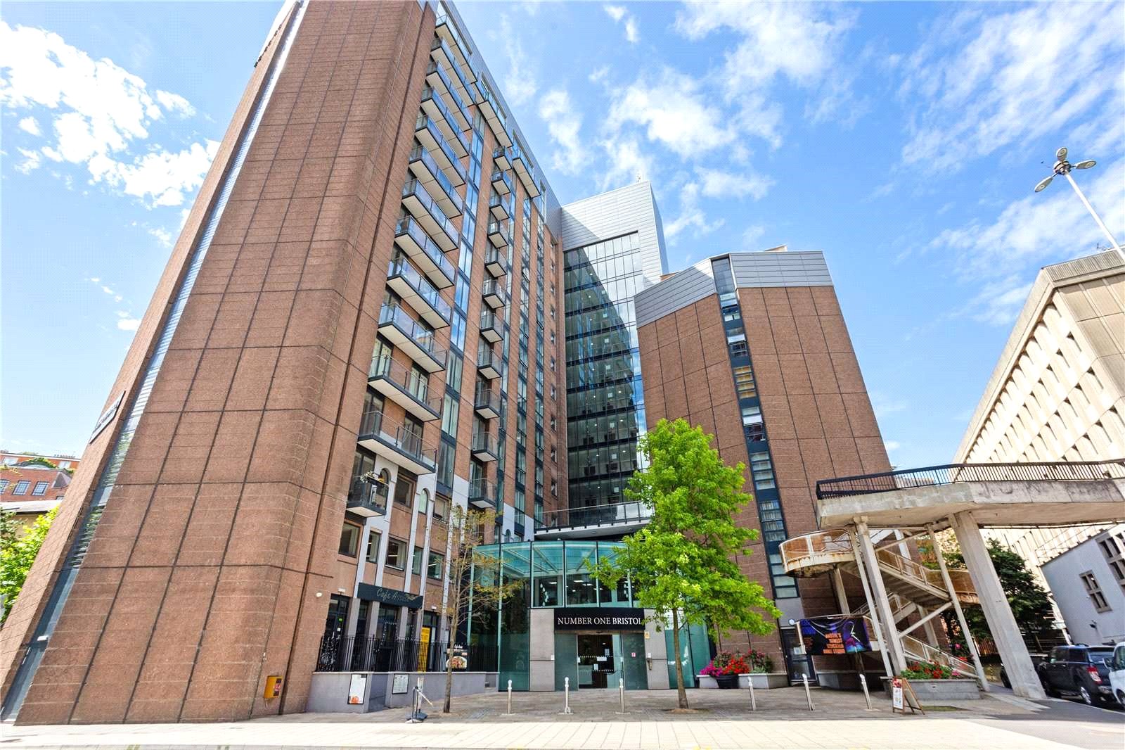 Modern high-rise building with glass facade and balconies, surrounded by other commercial structures.