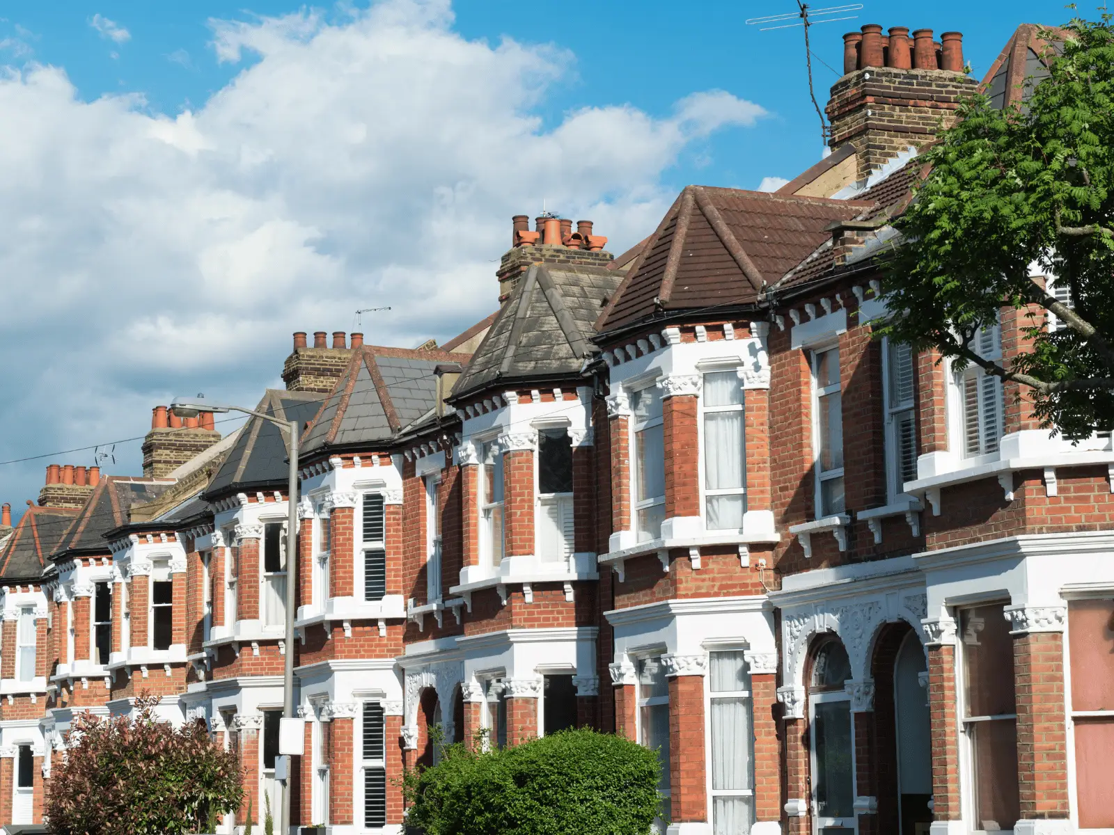 A row of Victorian-style red brick terraced houses with white ornate detailing, set against a blue sky with fluffy clouds.